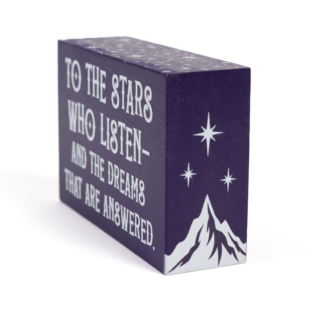 Side view of Purple wooden bookshelf sign reads ‘To the stars who listen and the dreams that are answered’ with a mountain and three stars on the sides and stars along the top, from ACOTAR by Sarah J Maas.