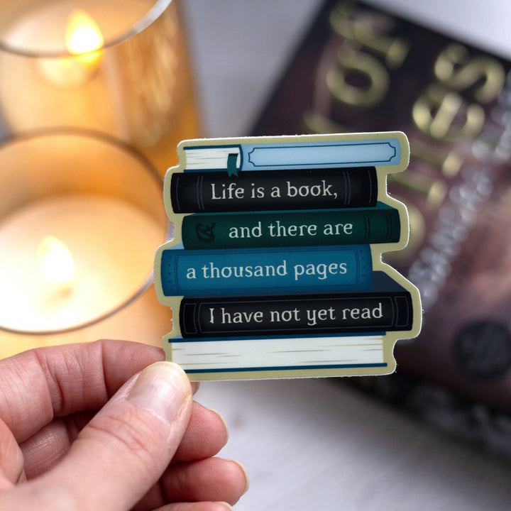 Sticker of a book stack with text on the spines reading ‘Life is a book, and there are a thousand pages I have not yet read’ held over City of Bones.