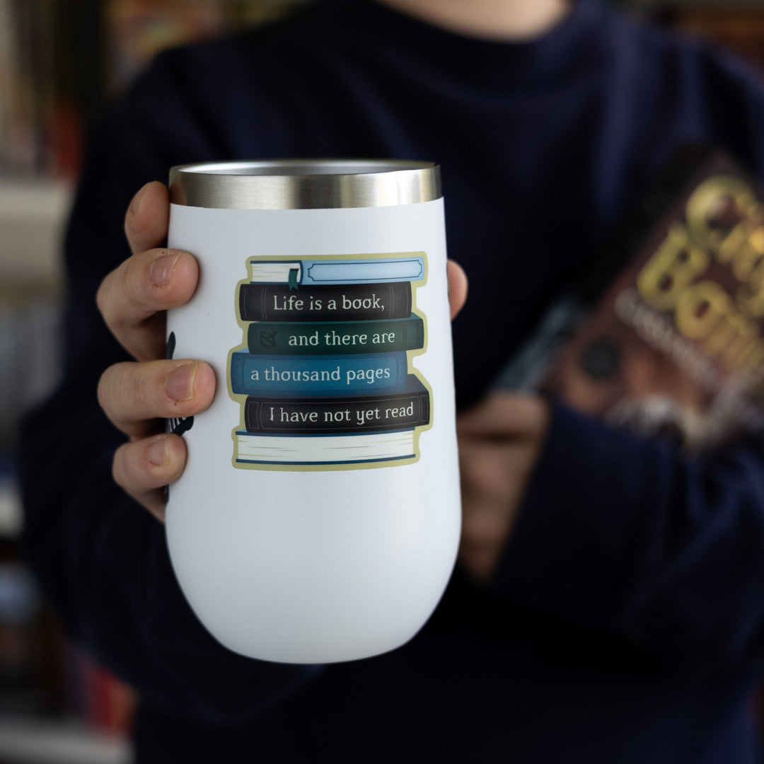 Sticker of a book stack with text on the spines reading ‘Life is a book, and there are a thousand pages I have not yet read,’ on a white tumbler.

