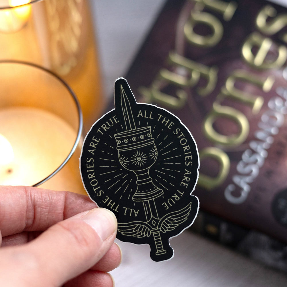  Sticker held over City of Bones that reads ‘All the stories are true,’ with the mortal sword and mortal cup from Shadowhunters by Cassandra Clare. 
