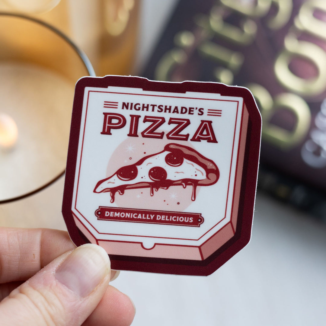  Sticker of pizza box reads ‘Nightshade’s pizza, demonically delicious’, held over City of Bones.
