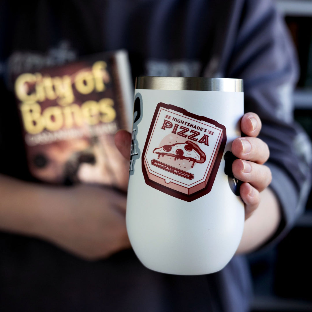 Sticker of pizza box reads ‘Nightshade’s pizza, demonically delicious’ from Shadowhunters by Cassandra Clare, on a white tumbler.