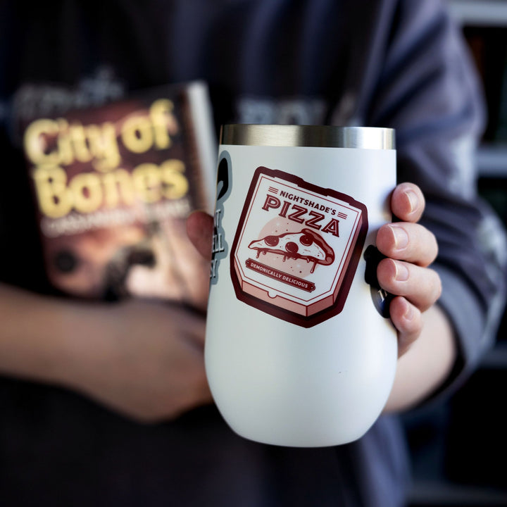 Sticker of pizza box reads ‘Nightshade’s pizza, demonically delicious’ from Shadowhunters by Cassandra Clare, on a white tumbler.