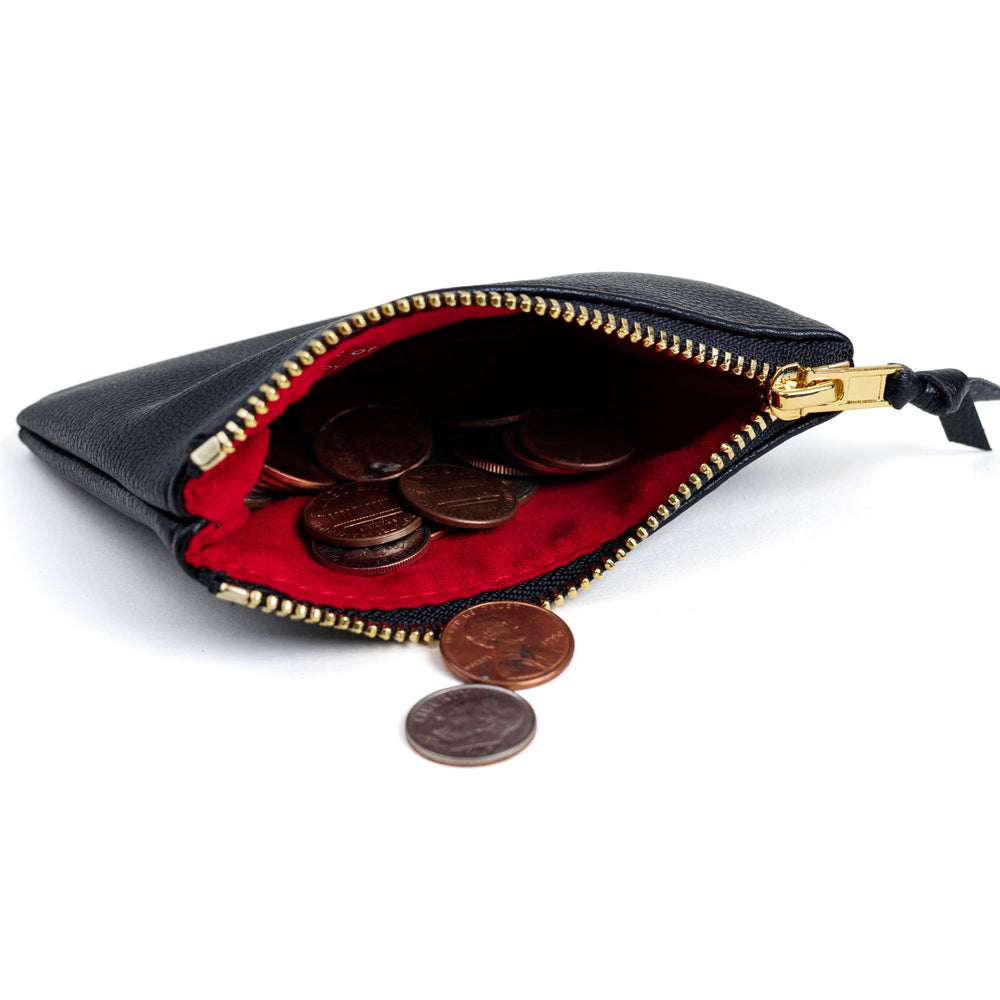   Small black coin purse with coins on its side and a red interior. 
