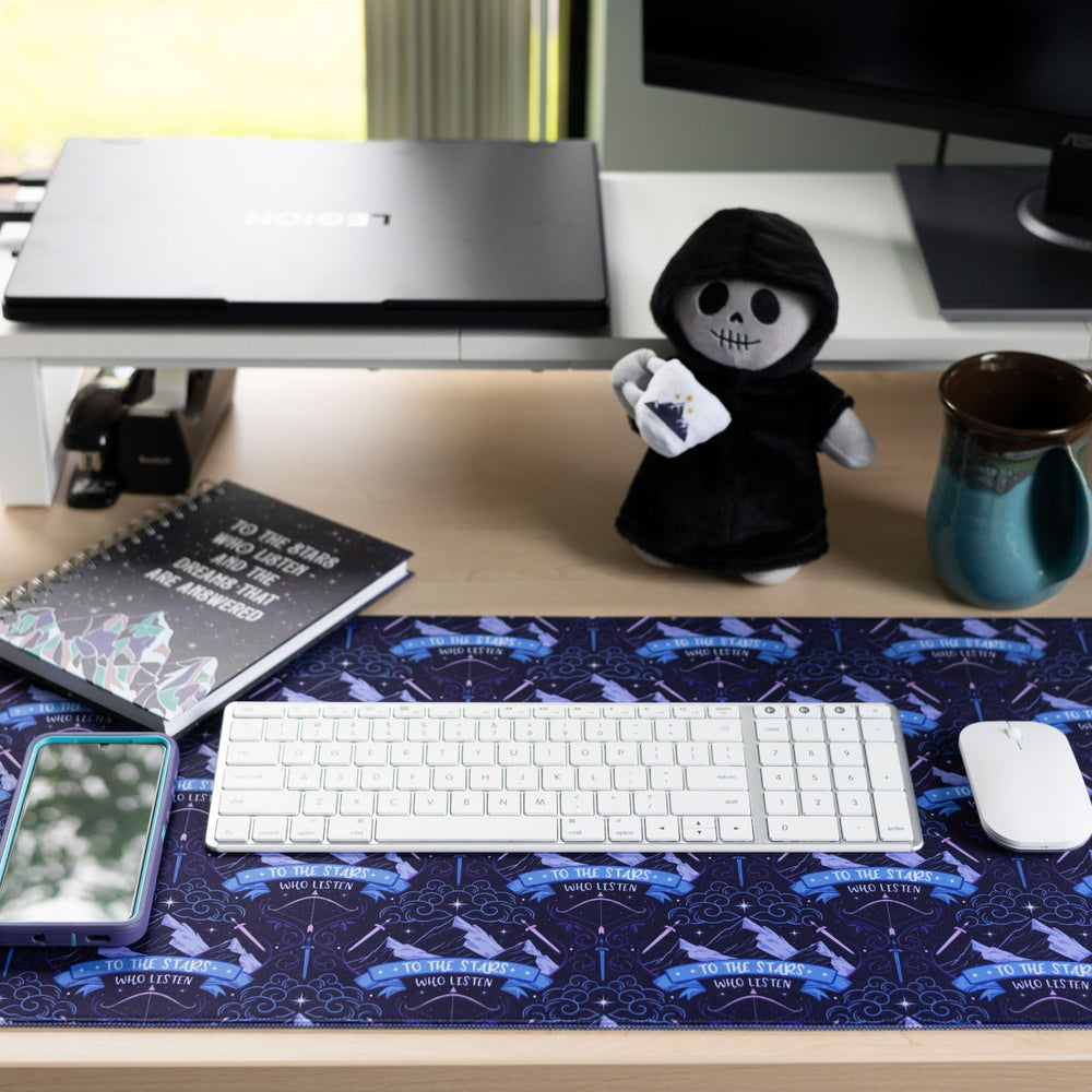 Desk mat on a desk with a pattern of Mt. Ramiel with swords on each side from ACOTAR and underneath reads ‘To the star who listen.’ , with a keyboard and mouse on top.