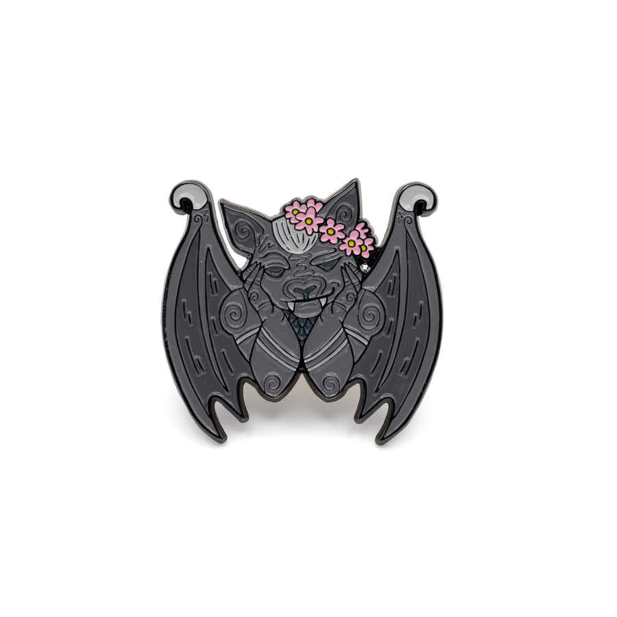 Enamel pin of a gargoyle in a flower crown, inspired by The Knight and the Moth. He is cradling his chin in his paws and smiling.