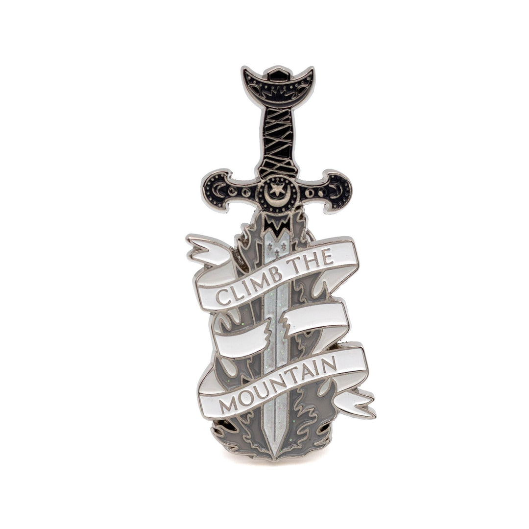Enamel pin of a sword with a sliced white ribbon around it that reads ‘ Climb the mountain’.