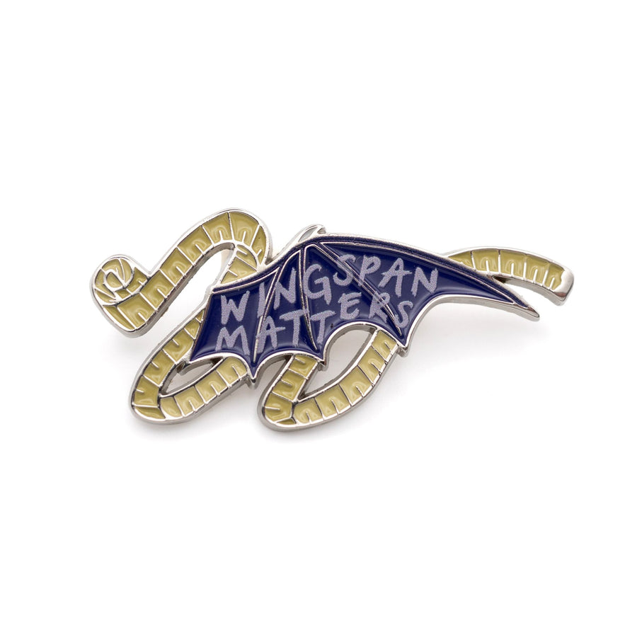 Enamel pin of a bat wing with measuring tape around it and on the wing it reads ‘wingspan matters’.