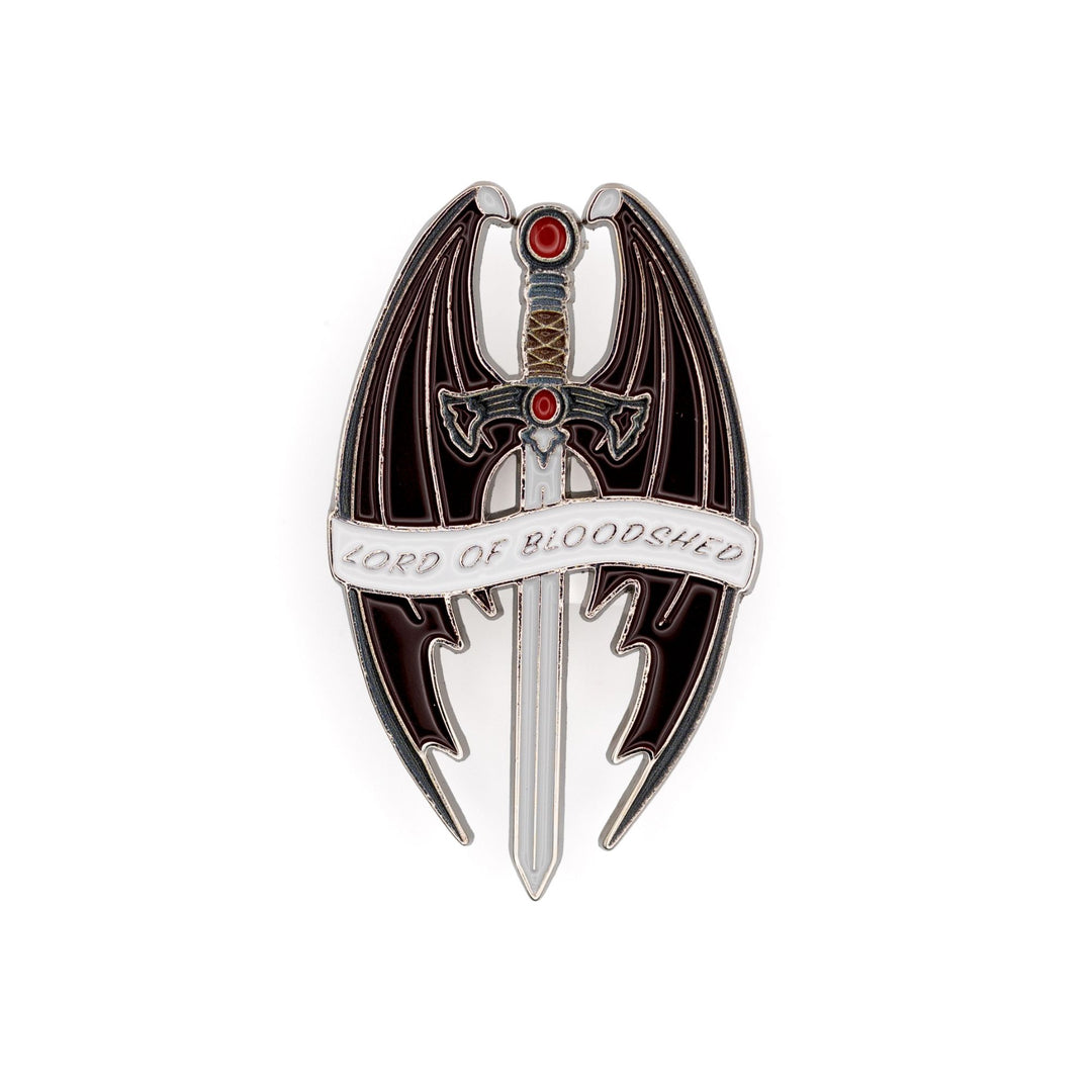 Enamel pin of a sword with a red stone and pommel, surrounded by bat wings that reads ‘Lord of Bloodshed’ on a white ribbon. 