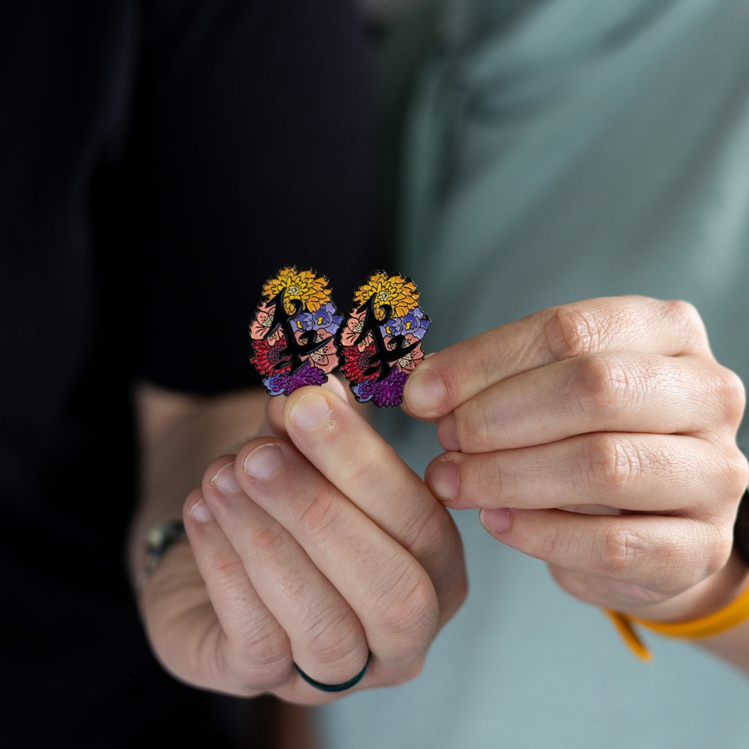  Black enamel pin of parabatai rune from Shadowhunters, surrounded by flowers being held together by two different hands.
