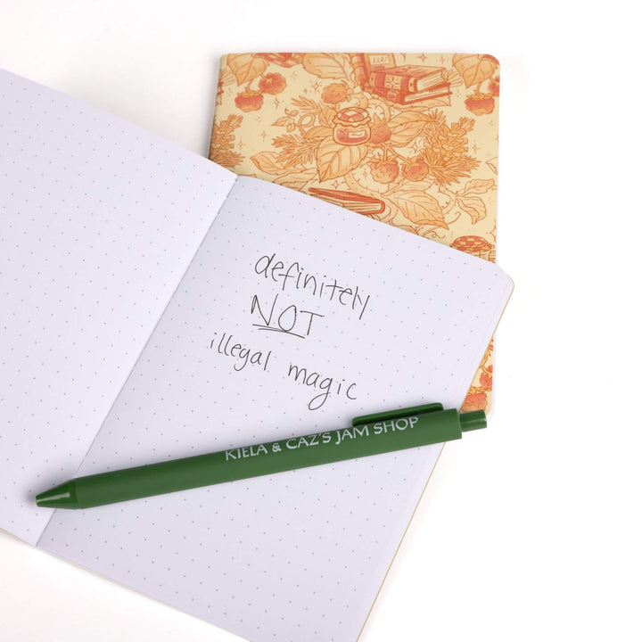  Strawberry & books A6 journal behind an open A6 dot grid journal with green pen and handwritten note: “Definitely not illegal magic.”