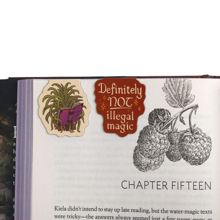 Caz the spider plant & “Definitely NOT illegal magic” magnetic bookmarks on open book. Character & quote from The Spellshop. 