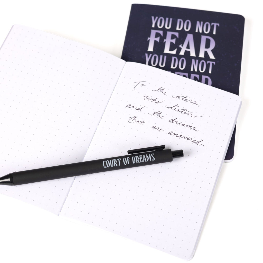 ‘You do not fear you do not falter you do not yield’ A6 journal behind an open A6 dot grid journal with black pen and handwritten note: To the stars who listen and the dreams that are answered.’