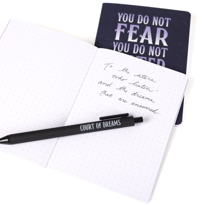 ‘You do not fear you do not falter you do not yield’ A6 journal behind an open A6 dot grid journal with black pen and handwritten note: To the stars who listen and the dreams that are answered.’