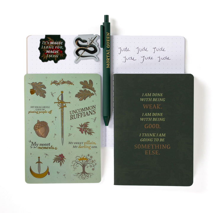 Gift set opened: Dot grid A6 journal open with pen, Serpent King Cardan & 'It’s magic I long for, magic I miss’ magnetic bookmarks, The Cruel Prince sticker sheet, A6 green ‘I am done being weak’ journal.
