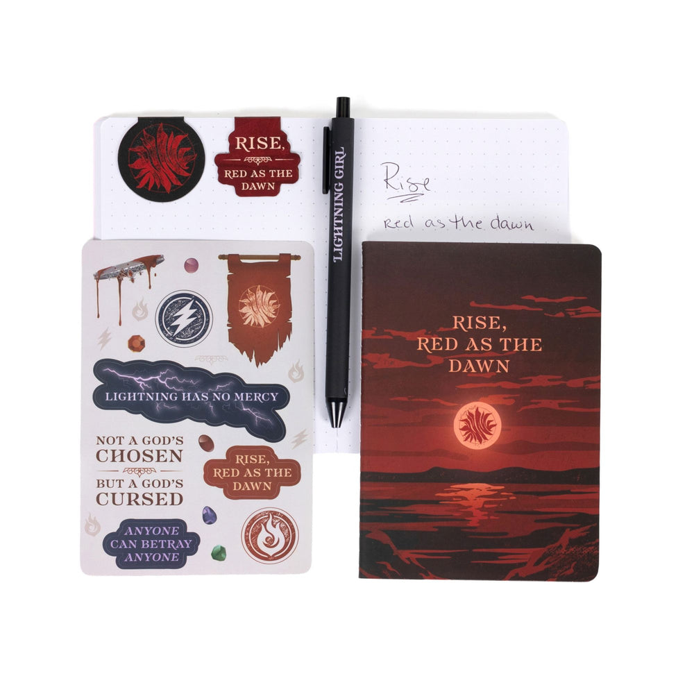 Gift set opened: Dot grid A6 journal open with pen, ‘Rise, Red as the Dawn’ and the Scarlet Guard insignia magnetic bookmarks, Red Queen sticker sheet, A6 ‘Rise, Red as the Dawn’ journal.