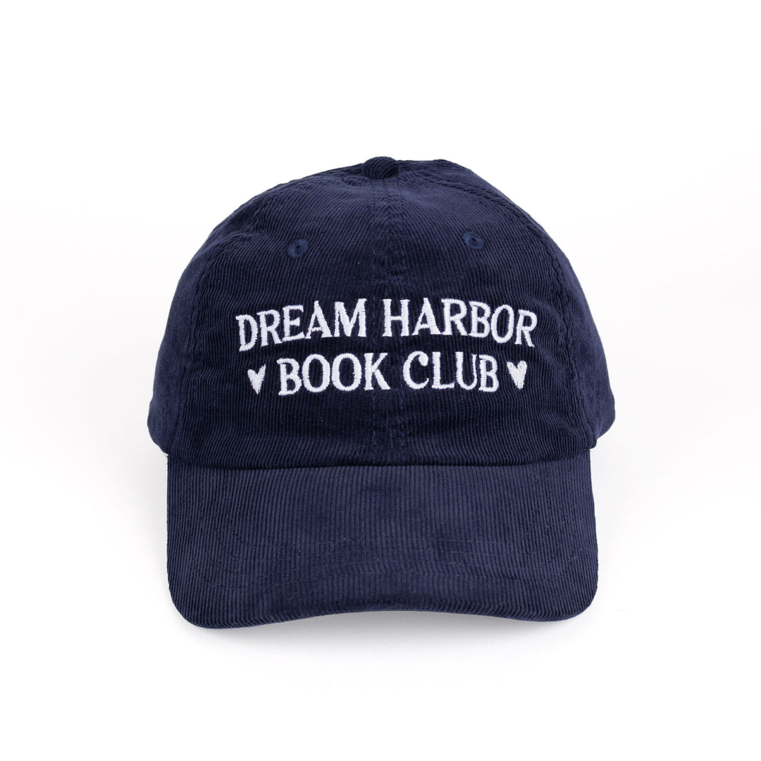 Dark blue, corduroy baseball cap with white embroidered text that reads ‘Dream Harbor Book Club.’ There are hearts around ‘Book Club.’