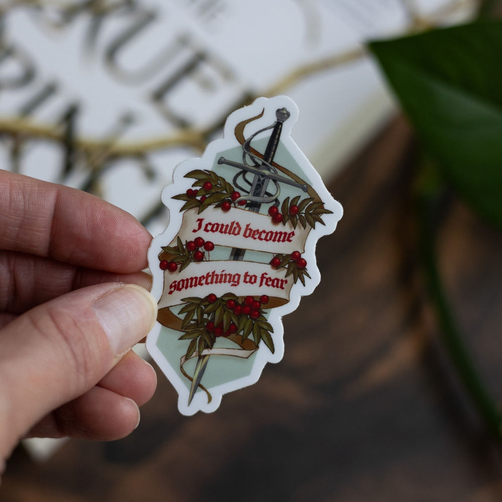 Sticker of the sword Nightfell with a banner ‘I could become something to fear’ and rowan berries, held above The Cruel Prince. 