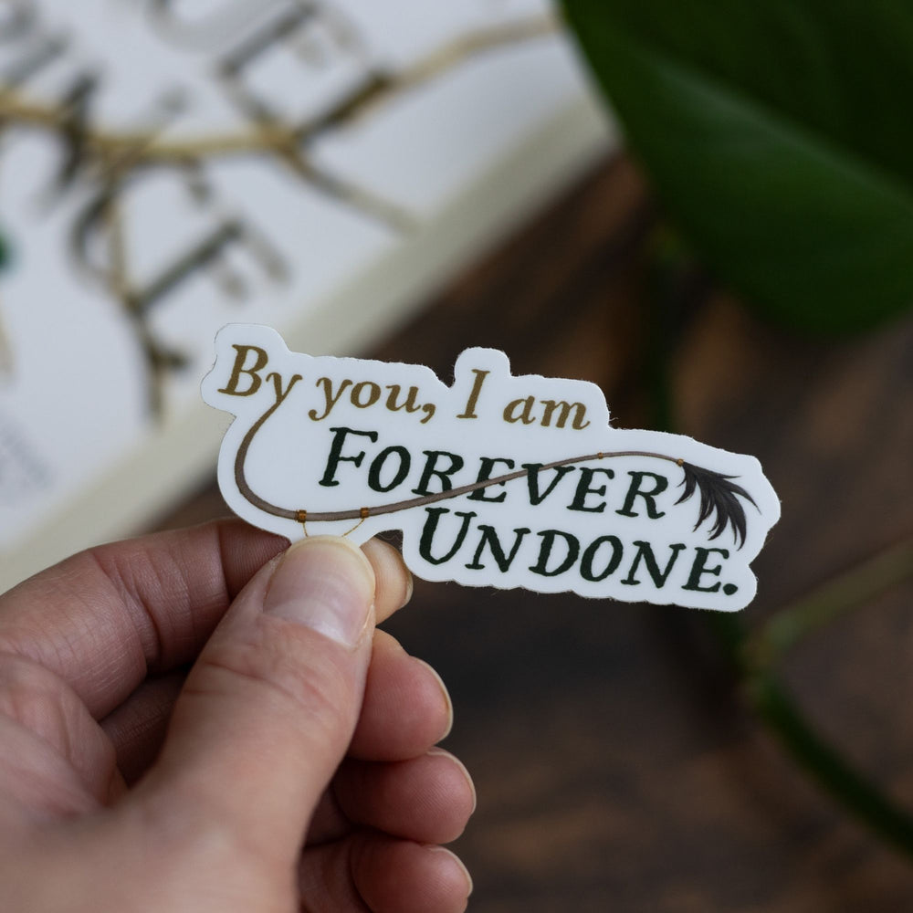 The Cruel Prince quote sticker: ‘By you, I am forever undone’ with Cardan’s tail. Held over The Cruel Prince. 