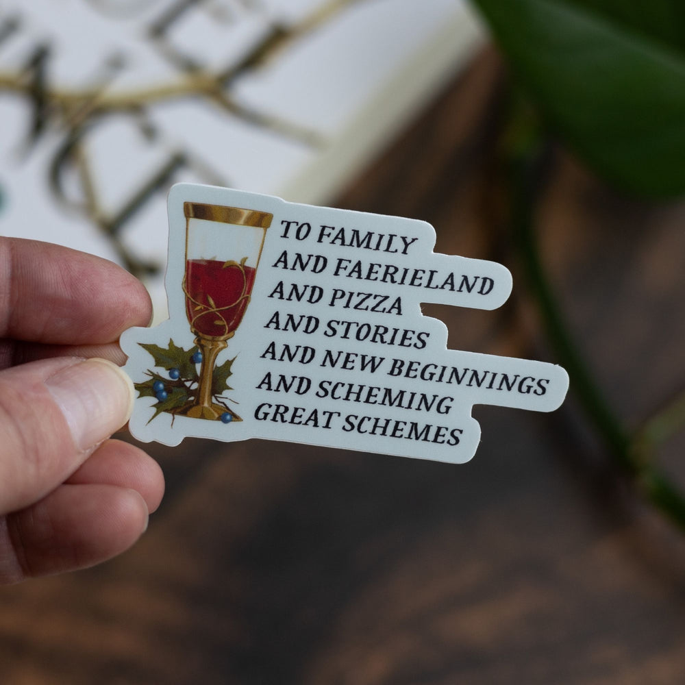 Cruel Prince quote sticker: ‘To family and faerieland and pizza and stories and new beginnings and scheming great schemes’ with a goblet. Held over The Cruel Prince.