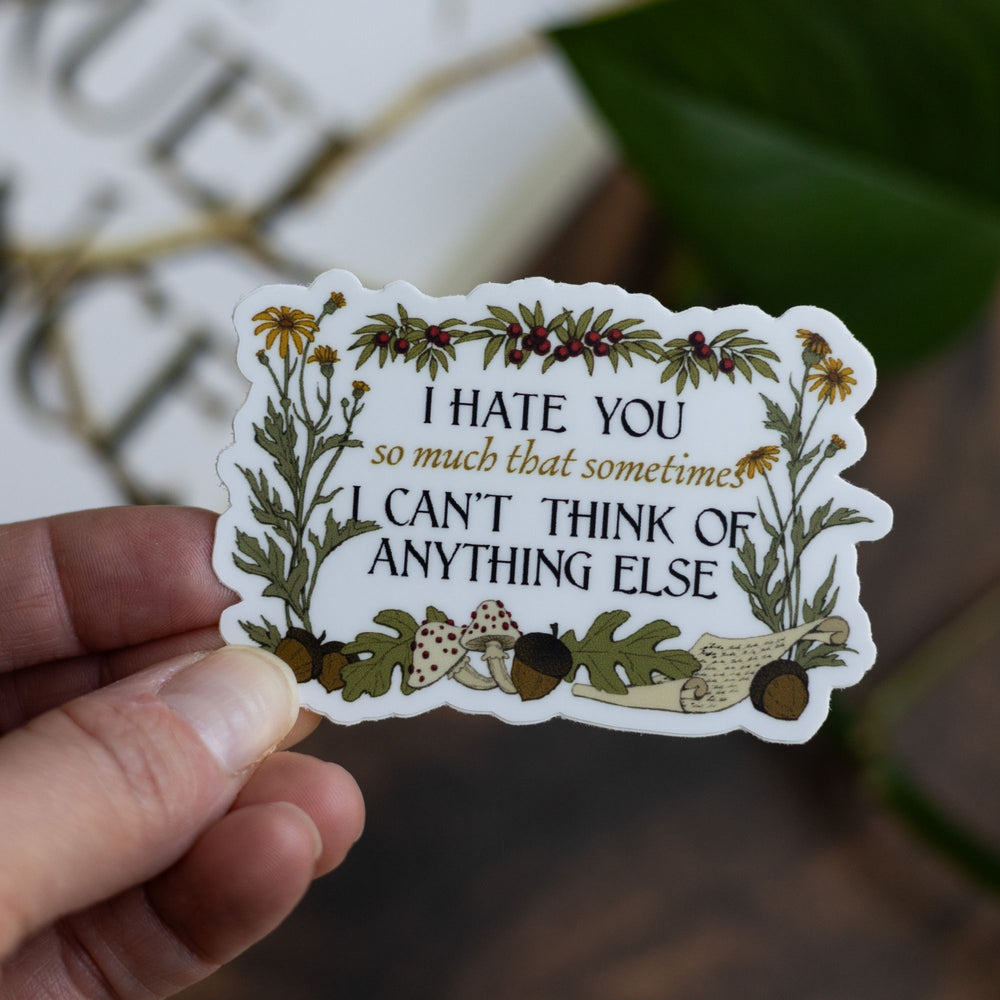 Cruel Prince quote sticker: ‘I hate you so much that sometimes I can’t think of anything else’ surrounded by plants. Held over The Cruel Prince.