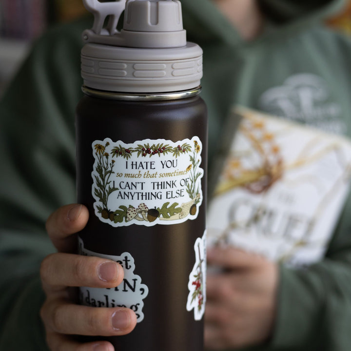 Cruel Prince quote sticker on black water bottle: ‘I hate you so much that sometimes I can’t think of anything else’ surrounded by plants.