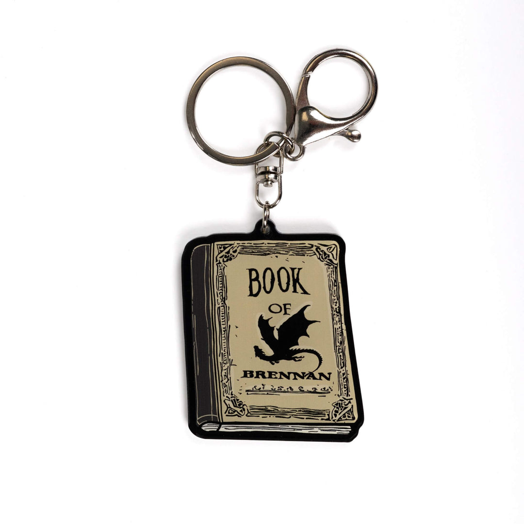 Acrylic keychain of the Book of Brennan from Fourth Wing. The book is parchment colored with black title text and a black dragon on the cover.

