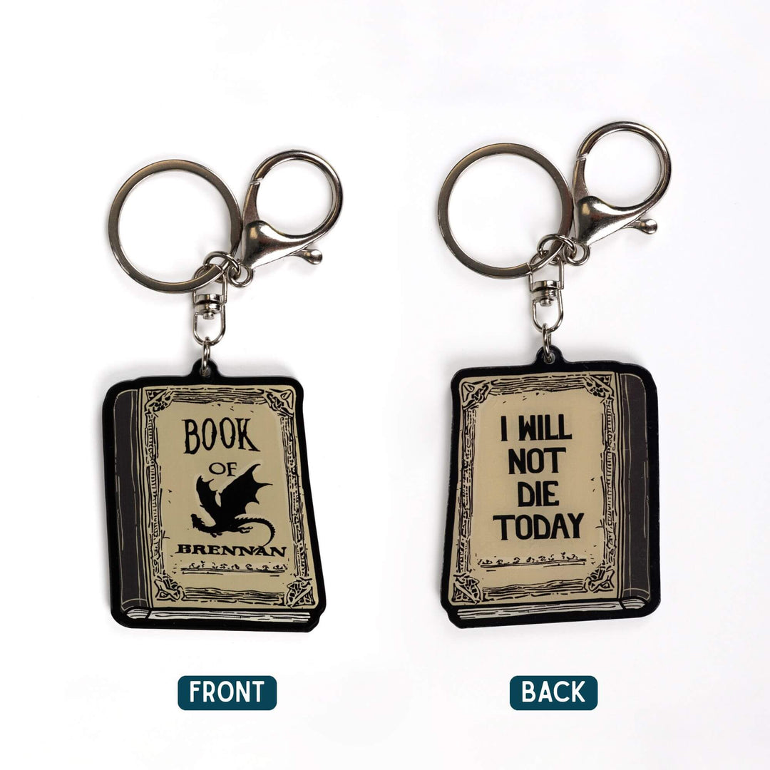 2 acrylic keychains, one of the Book of Brennan and the reverse side, the quote 'I will not die today.' Book is parchment color with black text.