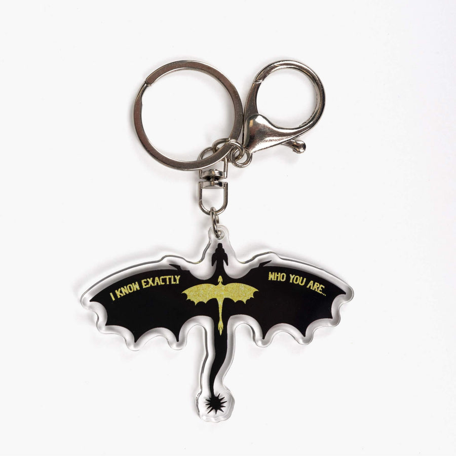 Acrylic keychain of the silhouette of a black dragon, wings spread, with a smaller glittery gold dragon overlaid. Quote on the wings is 'I know exactly who you are.'