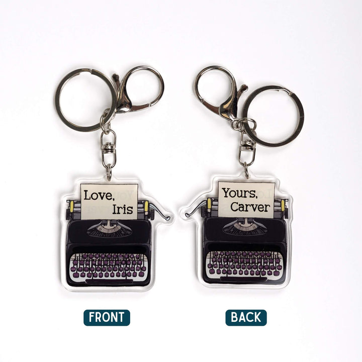 2 acrylic keychains of a black typewriter with paper in it. Photo shows both sides of the keychain. On one side the paper says 'Love, Iris.' And the other 'Love, Carver.'