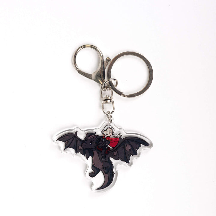 Acrylic keychain of a cartoon of the witch Manon riding Abraxos, her black wyvern