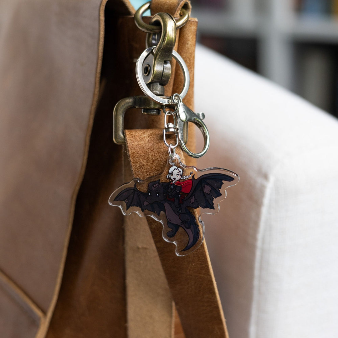  Acrylic keychain of a cartoon of the witch Manon riding Abraxos, her black wyvern clipped to a leather purse.
