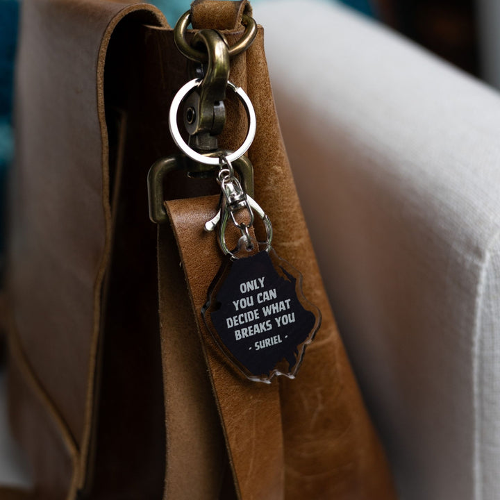 Acrylic keychain of the outline of a hooded figure clipped to a leather purse. Keychain says ‘Only you decide what breaks you.’
