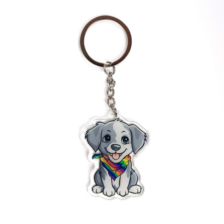 Acrylic keychain of a grey and white puppy, sitting happily and wearing a rainbow pride bandana.
