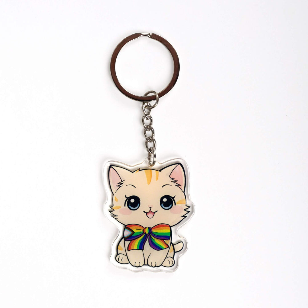 Acrylic keychain of a cream colored kitten with order stripes, sitting happily and wearing a progress pride flag bow tie.