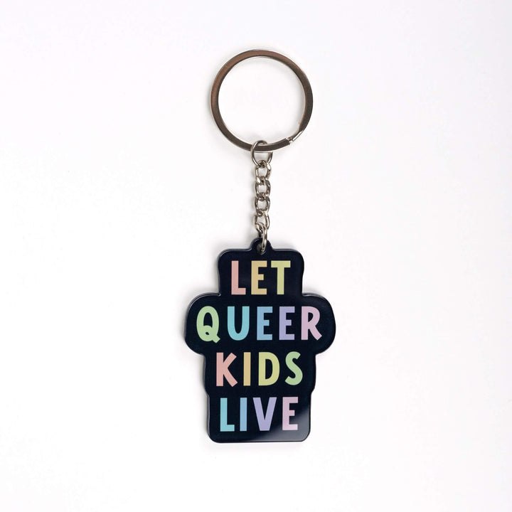 Acrylic keychain that says ‘Let queer kids live.’ The words are a pastel rainbow on a black background.