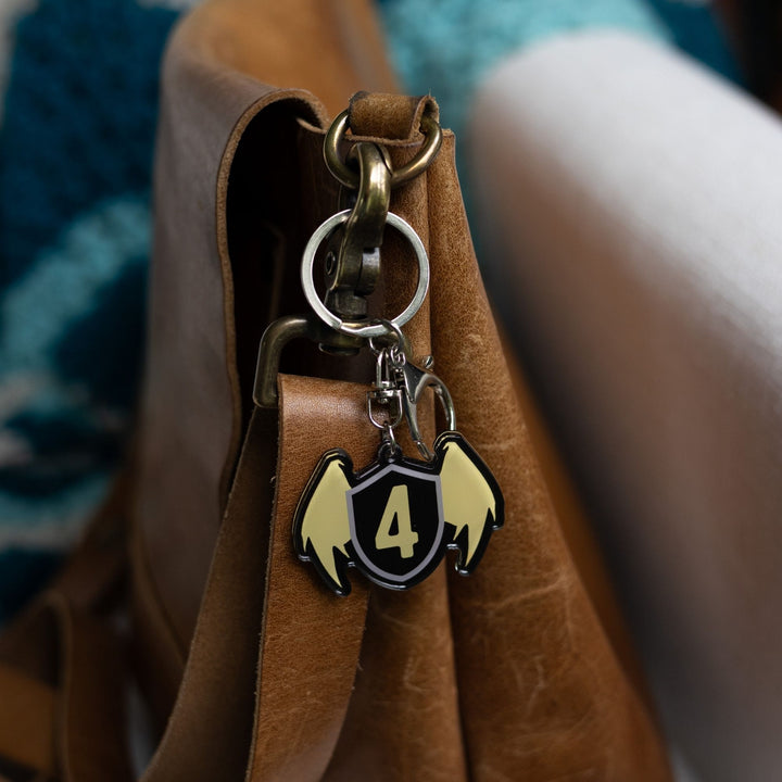 Acrylic keychain of a black shield with golden wings & a gold four on the shield clipped to a leather purse.