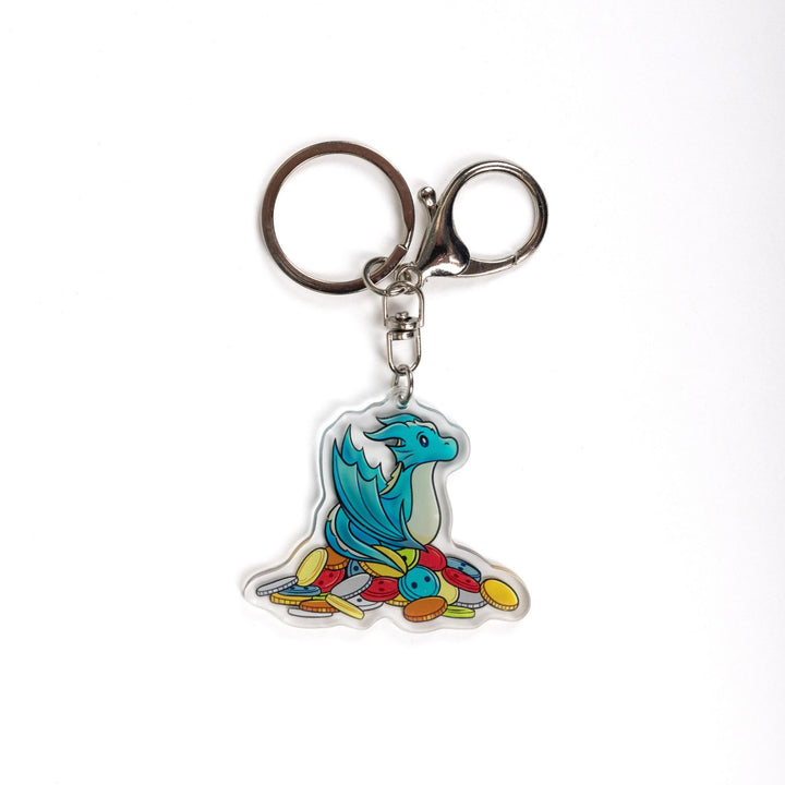 Acrylic keychain of Theodore, a blue baby wyvern, sitting on a pile of multicolored buttons from House in the Cerulean Sea. 
