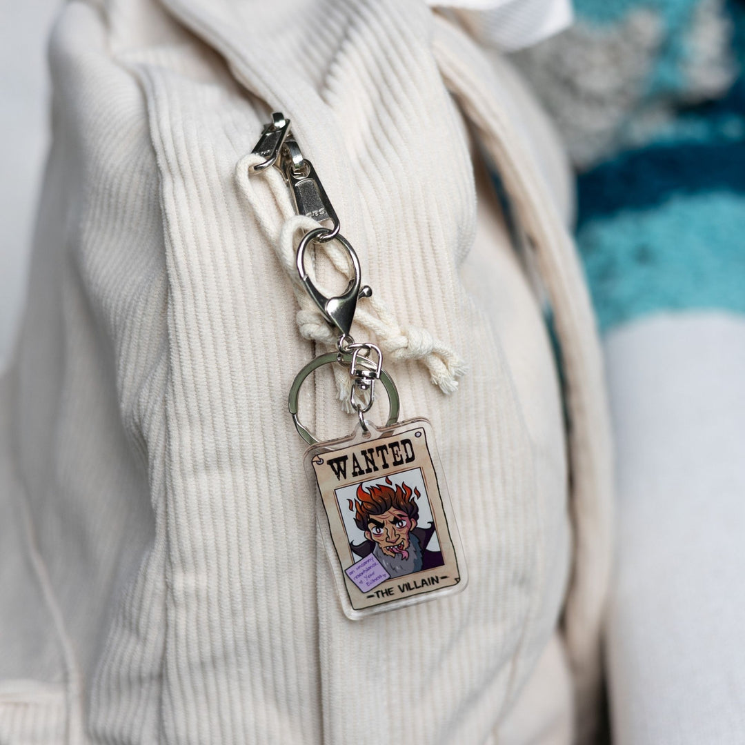  Acrylic keychain of a wanted poster of ‘The Villain’ With a purple post-it note on it that reads ‘An Uncanny resemblance, Your evilness’  clipped to a white backpack.