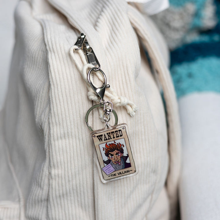  Acrylic keychain of a wanted poster of ‘The Villain’ With a purple post-it note on it that reads ‘An Uncanny resemblance, Your evilness’  clipped to a white backpack.