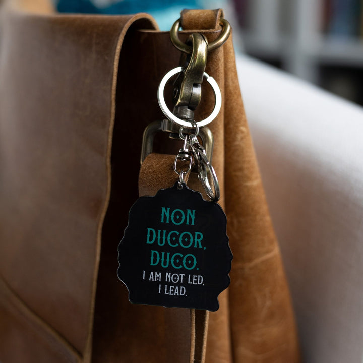 Keychain of a crest with the words ‘Non Ducor, Duco. I am not led, I lead’ clipped to a leather purse