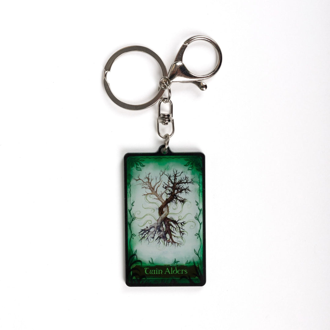 Acrylic keychain of a card with two trees intertwining on a green background. On the bottom it reads ‘Twin Alders’
