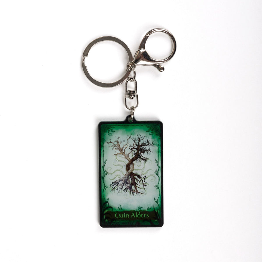 Acrylic keychain of a card with two trees intertwining on a green background. On the bottom it reads ‘Twin Alders’