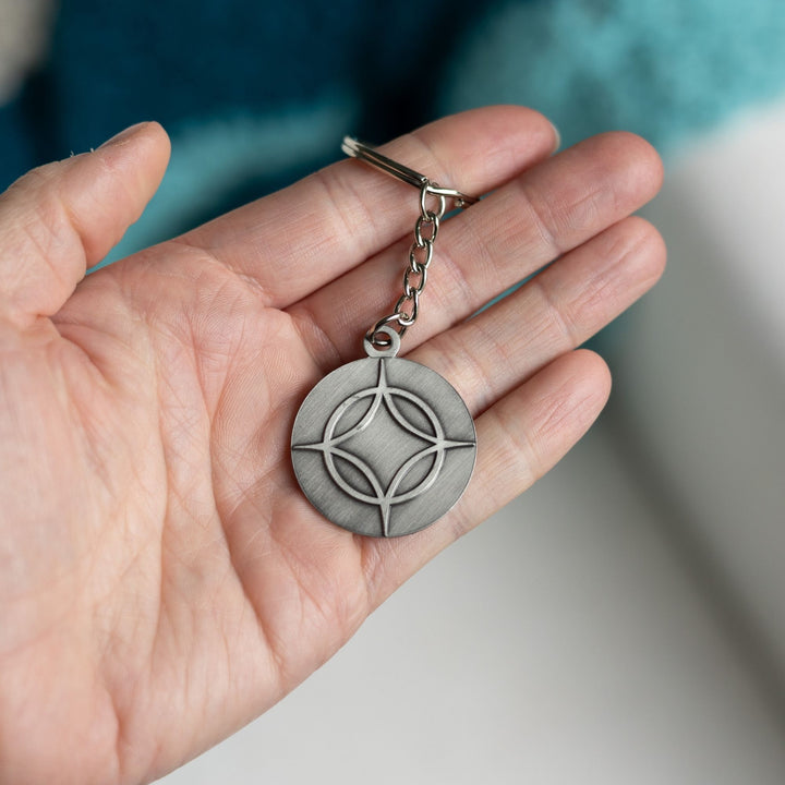 Metal keychain of a circle with a four point star over top. From Legendborn by Tracey Deonn. 
The backside has an etching of a dragon.
