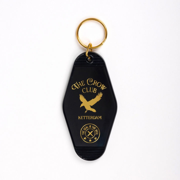  Black motel-style keychain with golden lettering and a golden crow for ‘The Crow Club. Ketterdam.’ ‘The deal is the deal’ in a small circle at the bottom.