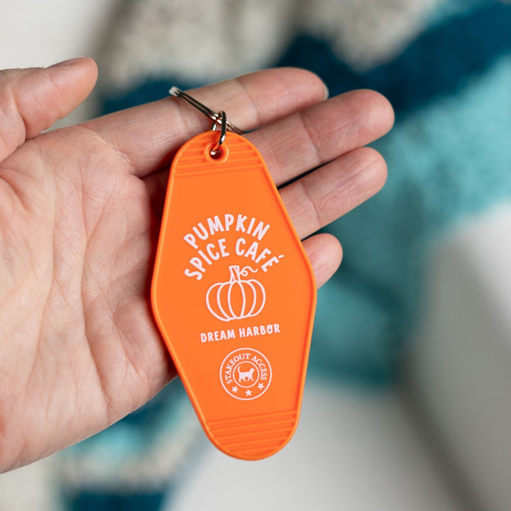  Orange motel-style keychain for ‘Pumpkin Spice Cafe. Dream Harbor’ in white letters with a pumpkin held in a palm. A circle under that says ‘Stakeout access.’