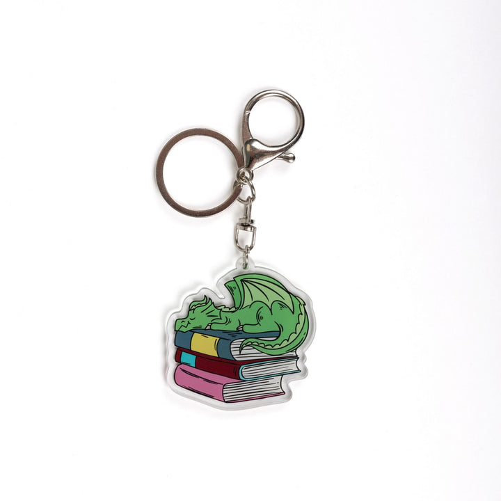  Acrylic keychain of a small green dragon asleep on a pile of books. 
