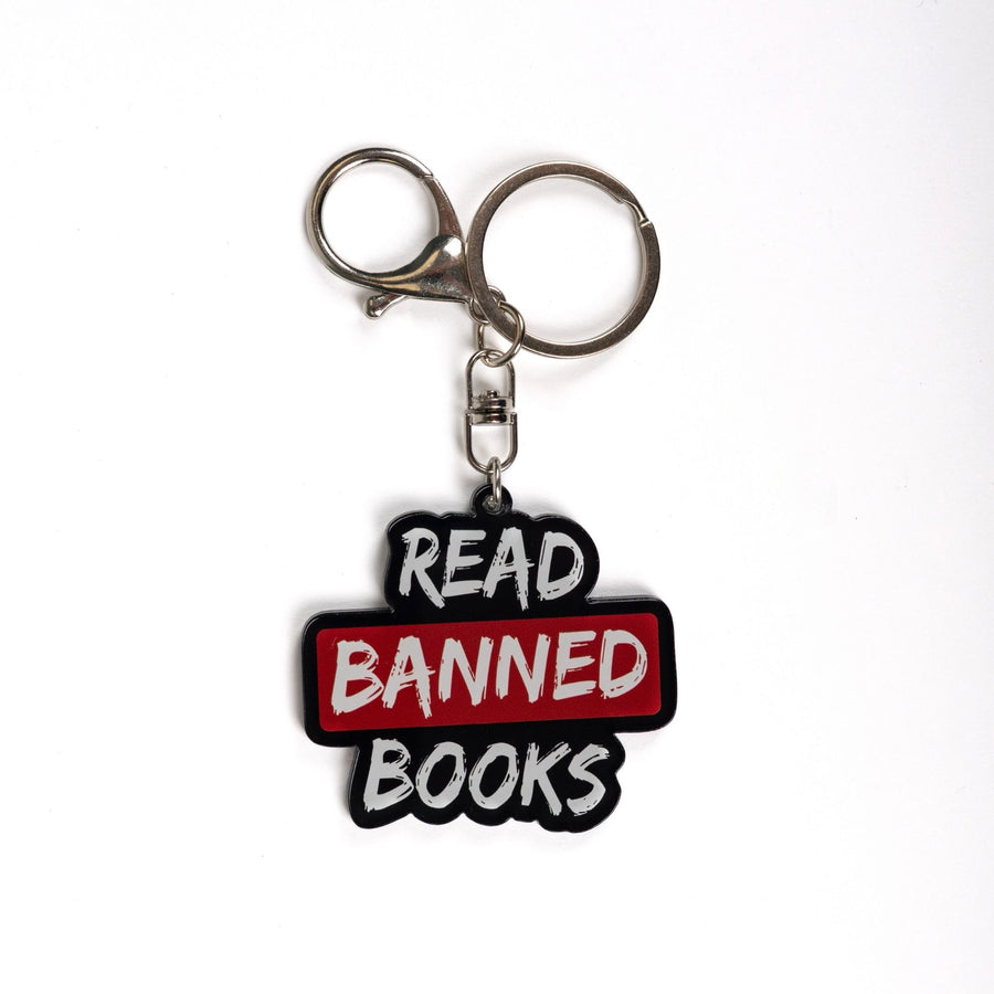Acrylic keychain that says ‘Read banned books’ in white lettering outlined in black. The word banned is red. 
