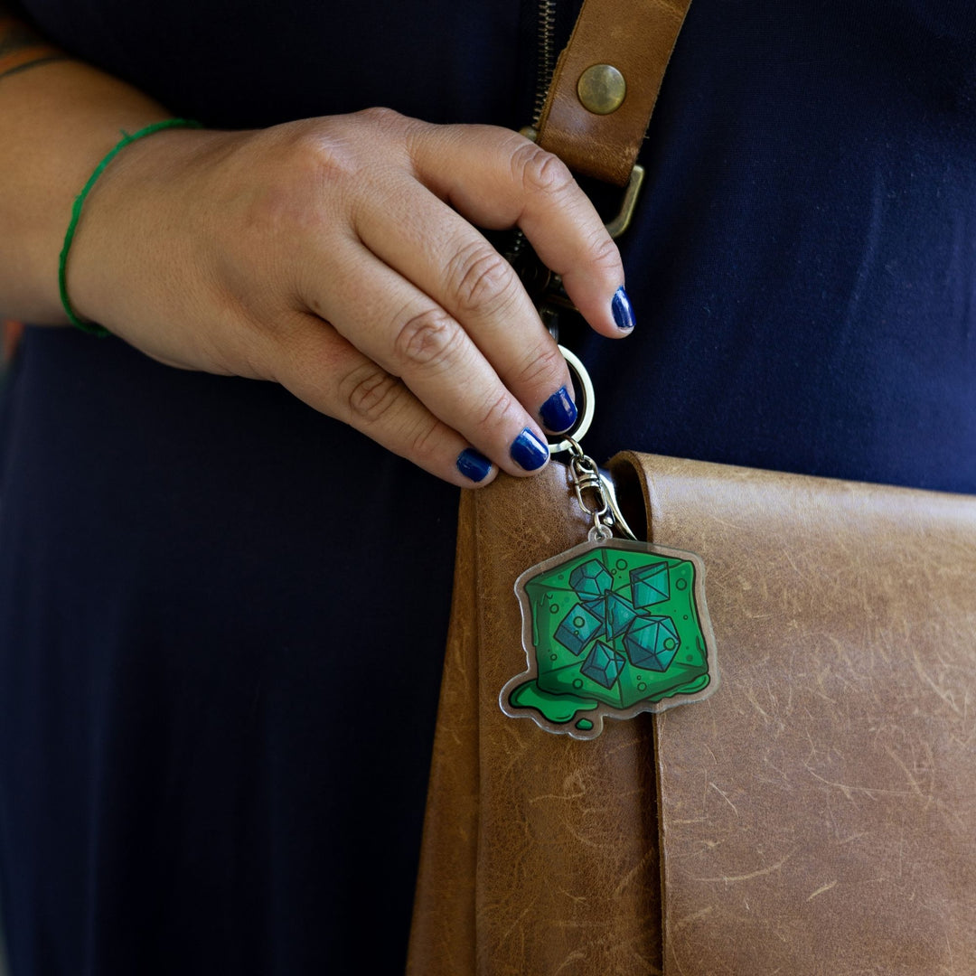  Acrylic keychain of a green gelatinous cube that is oozing and has DND dice inside of it clipped to a leather purse.
