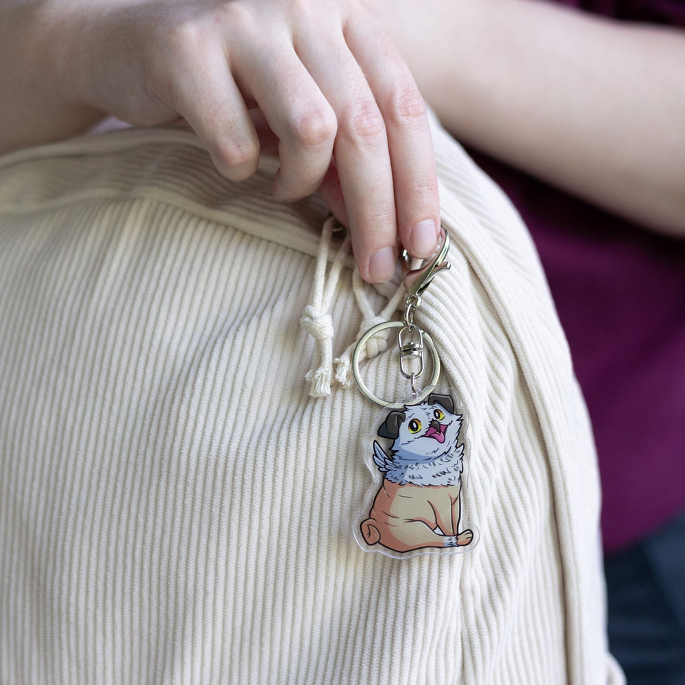 Acrylic keychain of Potroast, body and face of a pug with the beak and feathers of an owl  clipped to a white backpack. From Bookshops and Bonedust.